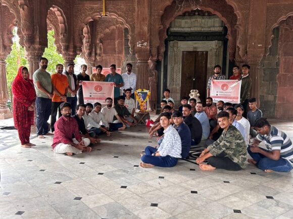 Ramdoot Restores volunteers sitting and standing inside a historic temple during a restoration gathering, holding banners.