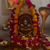 Sacred temple deity adorned with vibrant marigold and rose garlands, flanked by a brass Naga (serpent) idol.