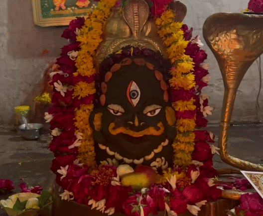 Sacred temple deity adorned with vibrant marigold and rose garlands, flanked by a brass Naga (serpent) idol.