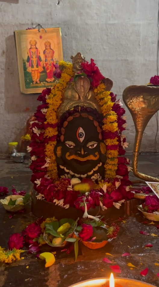 Sacred temple deity adorned with vibrant marigold and rose garlands, flanked by a brass Naga (serpent) idol.