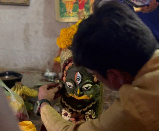 Devotee decorates a sacred Shiva Lingam with traditional elements and flowers during temple restoration rituals.