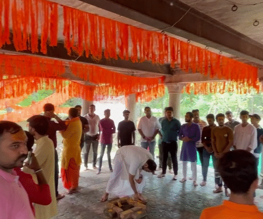 Community gathering during a havan ceremony under a decorated temple mandap with saffron festoons.