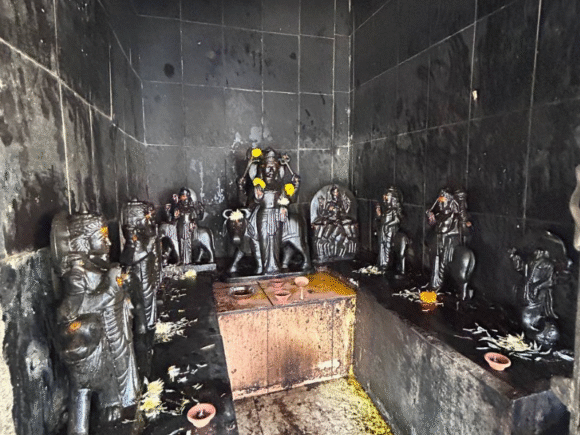 Black stone idols of deities inside a soot-covered shrine, with offerings of flowers and diyas, part of restoration efforts by Ramdoot Restores.