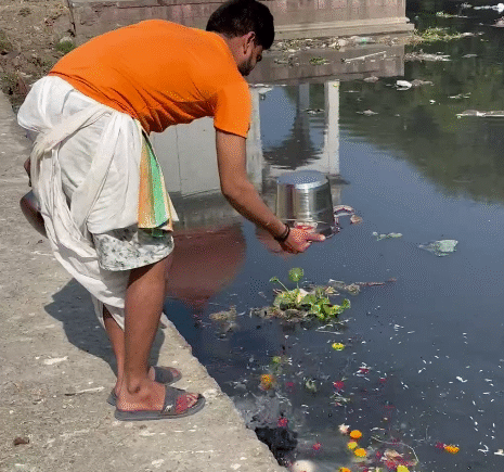 Man in traditional attire offering water and flowers into the river at Gangour Ghat, Indore, as part of a ritual; later cleaned by Ramdoot Restores volunteers.